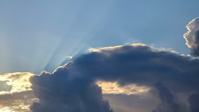 Sun rays breaking through thick dark storm clouds in sky