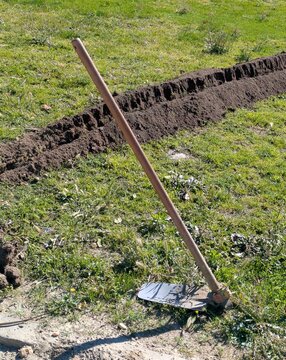 Trabajo agr&iacute;cola o de jardiner&iacute;a. Herramienta de jardiner&iacute;a tipo azada con mango de madera y cabeza met&aacute;lica, apoyada sobre el c&eacute;sped, con un surco de tierra detr&aacute;s 