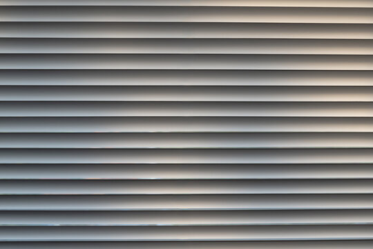 Modern white horizontal window blinds creating a clean geometric pattern with soft light and shadow. Minimalist architectural background ideal for interior design, textures and abstract concepts.
