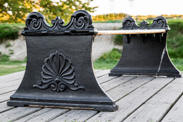 Obraz premium Vintage cast iron park bench with ornate decorative relief on a wooden platform outdoors