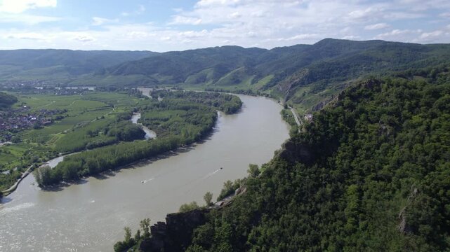 Aerial panoramic view of Danube River in Wachau Region of Lower Austria on clear summer day with prominent rock in foreground and small river boats travelling along river