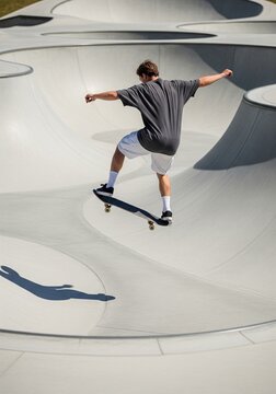 Back view of a young man flying high on a skateboard inside a concrete skatepark bowl