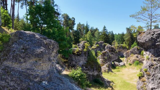 Luftaufnahme des Felsenmeers im Wental mit markanten Felsformationen aus Jurakalk, umgeben von einem dichten Nadelwald und Wanderwegen auf der Schw&auml;bischen Alb bei Sonnenschein.