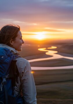 A happy woman hiker with a backpack looking at a beautiful sunset over a winding river valley