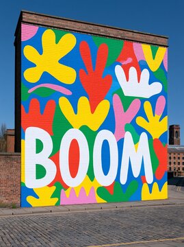 A brick wall painted in a vivid and colorful abstract floral pattern with the all-caps word "Boom" painted along the bottom left corner edge