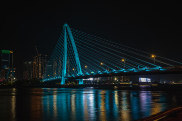 Fototapeta premium Ba Son Bridge with pink and purple LED illumination reflected in Saigon River at night, Ho Chi Minh City, Vietnam