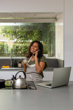 Hispanic woman talking on smartphone while working in modern kitchen