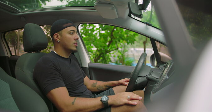 Latin Hispanic man sitting quietly inside parked car, looking out through windshield with calm and reflective expression, appearing lost in thought or waiting in traffic