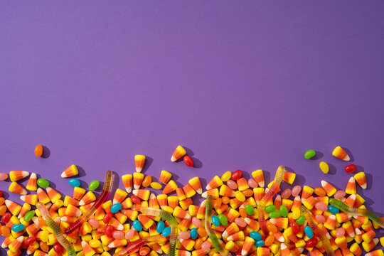 Happy Halloween candy assortment with candy corn and gummy worms on purple background