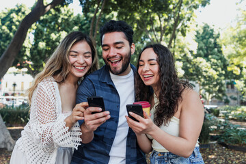 Fototapeta premium group of latin friends holding and using phone in public park in Mexico Latin America, hispanic people having fun 