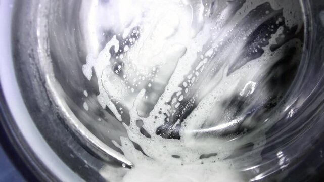 Close up of washing machine glass door with soapy foam spinning during laundry cycle. Washing dark or black clothes, color renewal process