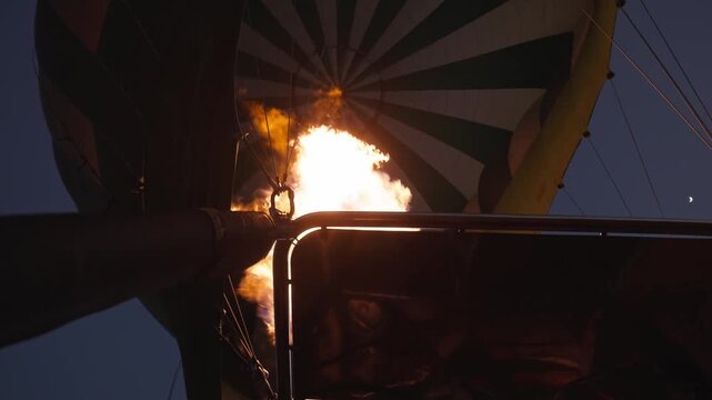 Slow motion in early morning darkness of hot air balloon fire, chemicals, liquid propane gas, and air rising as balloons rise for dusk ride through the sky on tourist adventure as flames shoot up 4k