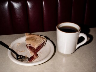 Obraz premium Candid lo-fi 35mm film snapshot of half eaten pie and black coffee cup on retro diner table