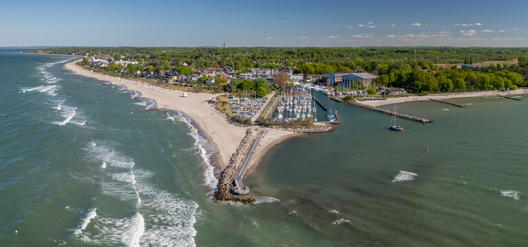 Aerial drone shot showcases the scenic coastline of Niendorf at Timmendorfer Strand, featuring a small marina full of sailboats, protective stone breakwaters, sandy beaches