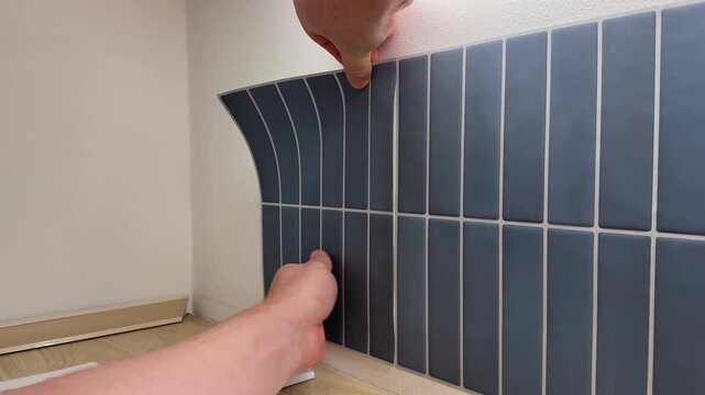 Hand applies flexible blue tile sheet to wall in home interior, close view of diy renovation work, clean modern surface suggests practical improvement