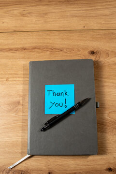 the concept of gratitude with a blue sticky note, a pencil and a closed notebook, the message on the sticky note is thank you.