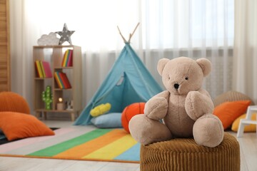 Cute toy bear on pouf in stylish child's room, closeup. Space for text © New Africa