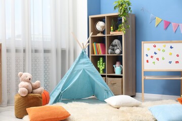 Blue wigwam, colorful pillows, pouf and shelving unit in stylish child's room. Interior design © New Africa