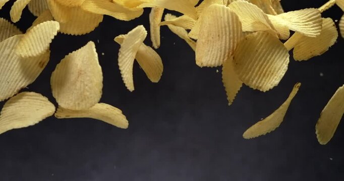 Ridged potato chips falling in slow motion on black background