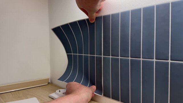 Hands apply flexible blue tile sticker on bathroom wall, close up home renovation detail, clean modern interior, practical diy improvement and decor upgrade