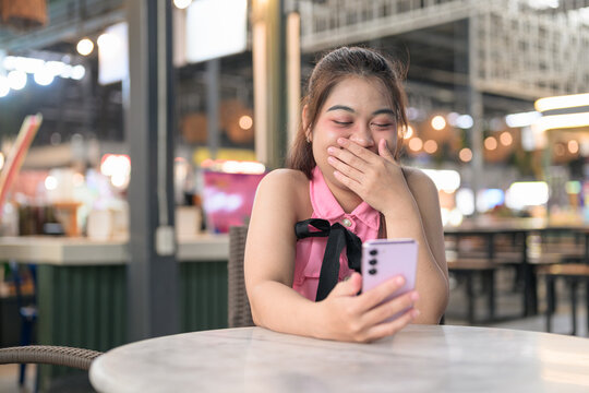 Amused Thai Isan woman laughing while reading a message on her smartphone