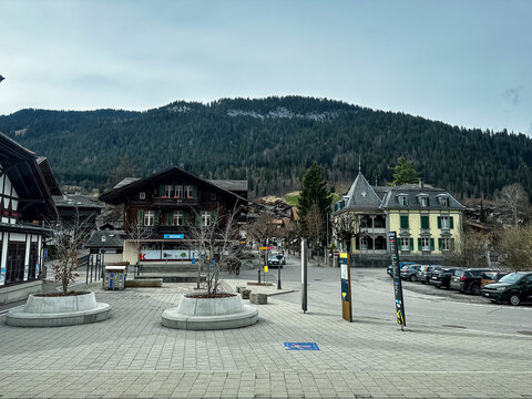 Gstaad, Switzerland - 11.03.2026. High-angle perspective of the public cobblestone plaza (Bahnhofplatz) outside the Gstaad train station in Switzerland. The upscale alpine resort scene features tradit