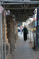 Fototapeta premium Pedestrians walking under metal construction scaffolding on a city sidewalk in Warsaw