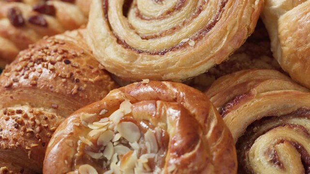 assorted freshly baked sweet pastries rotating on a dark wooden table closeup, food background. Selection of golden brown bakery buns