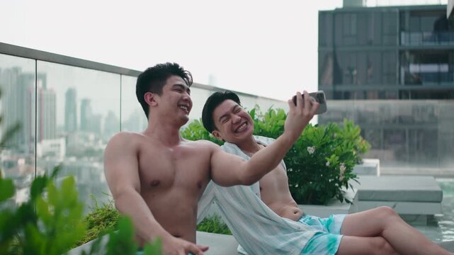 Gay couple taking a smartphone selfie at a rooftop pool in the city