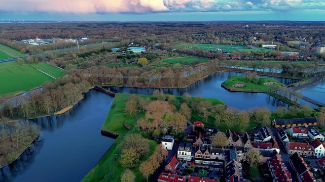 Aerial wide angle panoramic view of a historic star fort fortress with sharp zig-zag canals green ramparts old stone bastions and bunker entrances under a sunset storm sky
