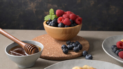 Wooden Bowl Filled with Fresh Raspberries and Blueberries Next to a Small Cup of Honey © homydesign