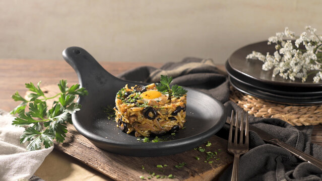 Traditional Portuguese Bacalhau a Bras Plated with Black Olives and Egg Yolk in a Black Skillet