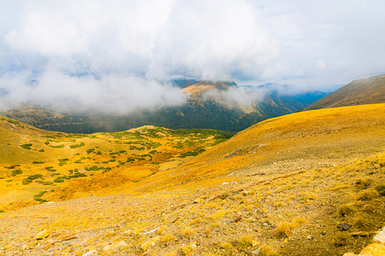 Golden rolling alpine tundra valley covered in low clouds and sweeping fog on a cool autumnal day in Rocky Mountain National Park, Colorado.