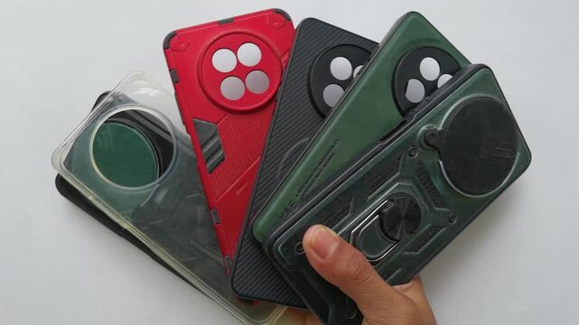 A hand holding a variety of protective smartphone cases in different colors and designs against a white background.