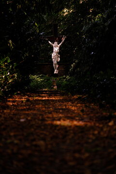 Atmospheric stone crucifix statue in deep autumn forest shadows