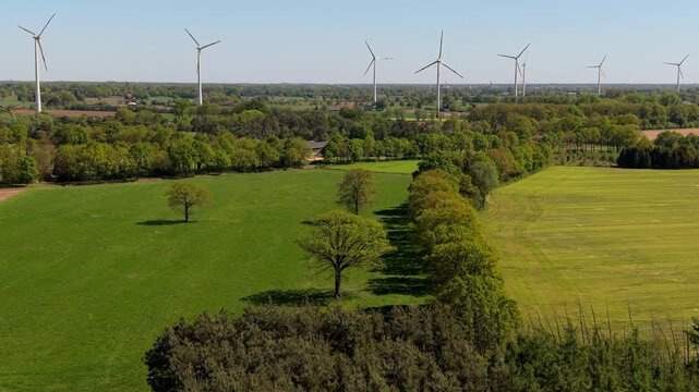 Aerial wide angle panoramic view of vast green agricultural fields and a row of modern wind turbines generating renewable energy in the countryside under a clear blue sky