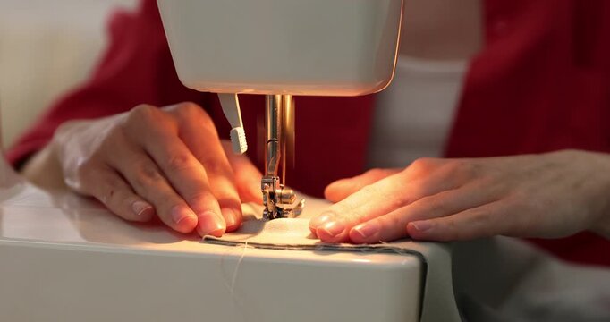 Woman sewing fabric with professional machine at table in workshop, closeup