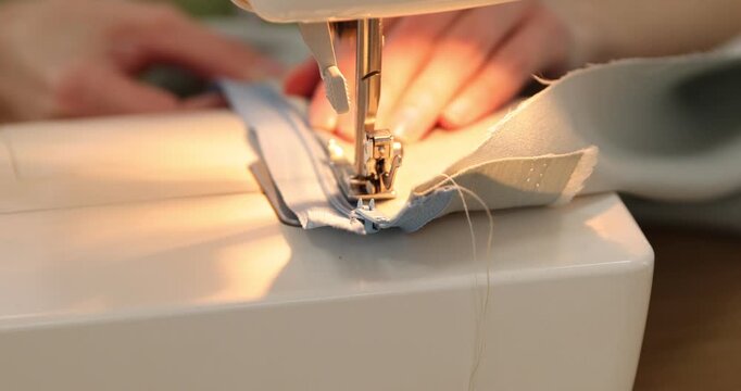 Woman sewing fabric with professional machine at wooden table in workshop, closeup