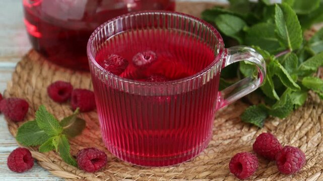 Woman adding fresh berries and mint to aromatic raspberry tea at wooden table, closeup