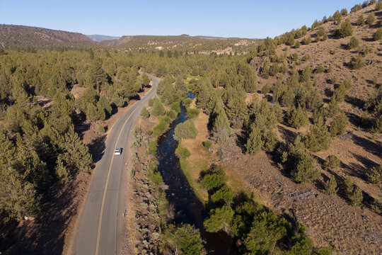 Aerial drone view of a car on Jess Valley Road alongside the Pit River in Modoc County, California through juniper forest.