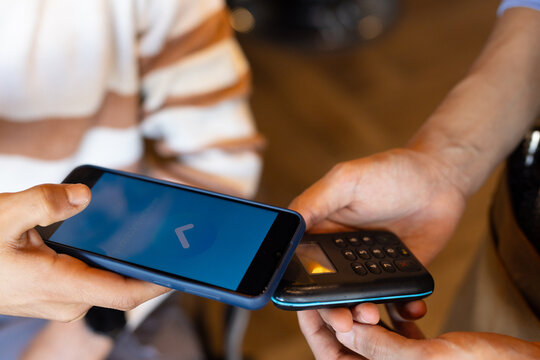 Two African American men exchanging contactless payment at cafe counter with phone and terminal