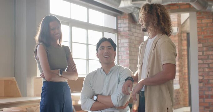 Three coworkers standing and talking in loft studio, seated man on stool starting chat sharing joke