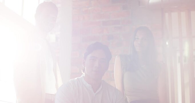 Diverse coworkers posing for team shot by big window, sunlight flooding lens, washing then clearing