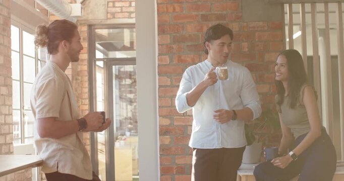 Diverse coworkers chatting after Asian man sipping glass mug by brick wall and window during break