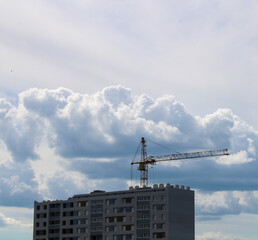 Fototapeta premium Construction of an apartment building with a tower crane and clouds in the background