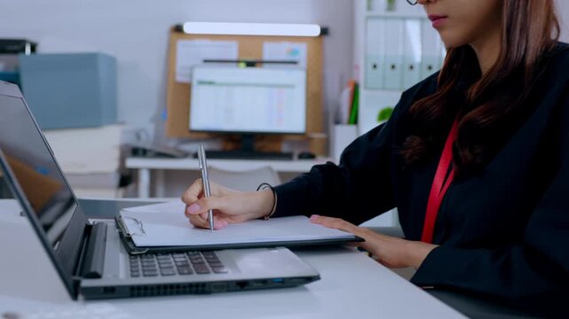 Businesswoman laptop notebook pen office desk writing workspace computer professional working with documents clipboard eyeglasses in modern workplace focused productivity setup