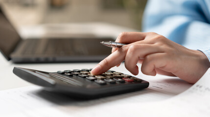 Businesswoman calculating tax and financial data with calculator and laptop, reviewing charts and...