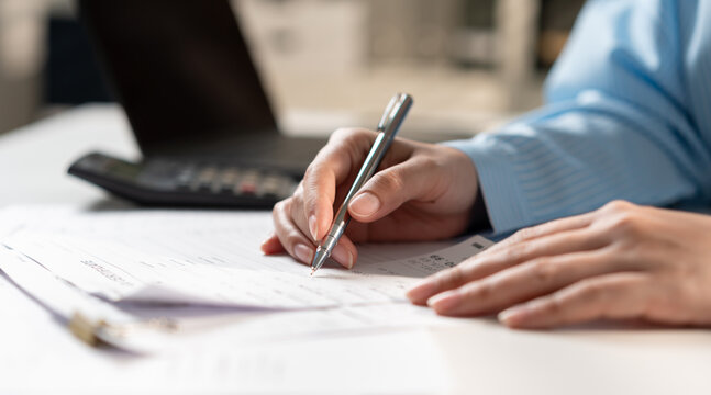 Close up of businesswoman hand writing on tax form at office desk. Accountant auditing financial invoice receipt, calculating budget or corporate management concept.