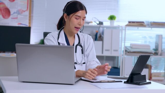 Asian doctor woman in clinic office with laptop tablet stethoscope medical physician at desk consulting online, taking notes, healthcare worker using digital device clipboard calmly under stress