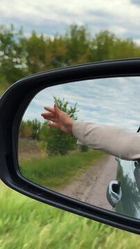 Travel road trip woman hand flying air wind at car back mirror slow motion VERTICAL VIDEO. Freedom female arm automobile driving speed movement lifestyle vacation weekend summer green tree highway